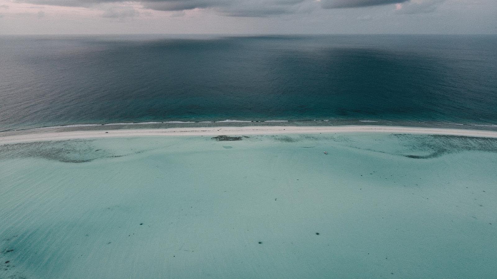 Aerial view of a Maldives atoll edge where the reef drops into open water at dusk.