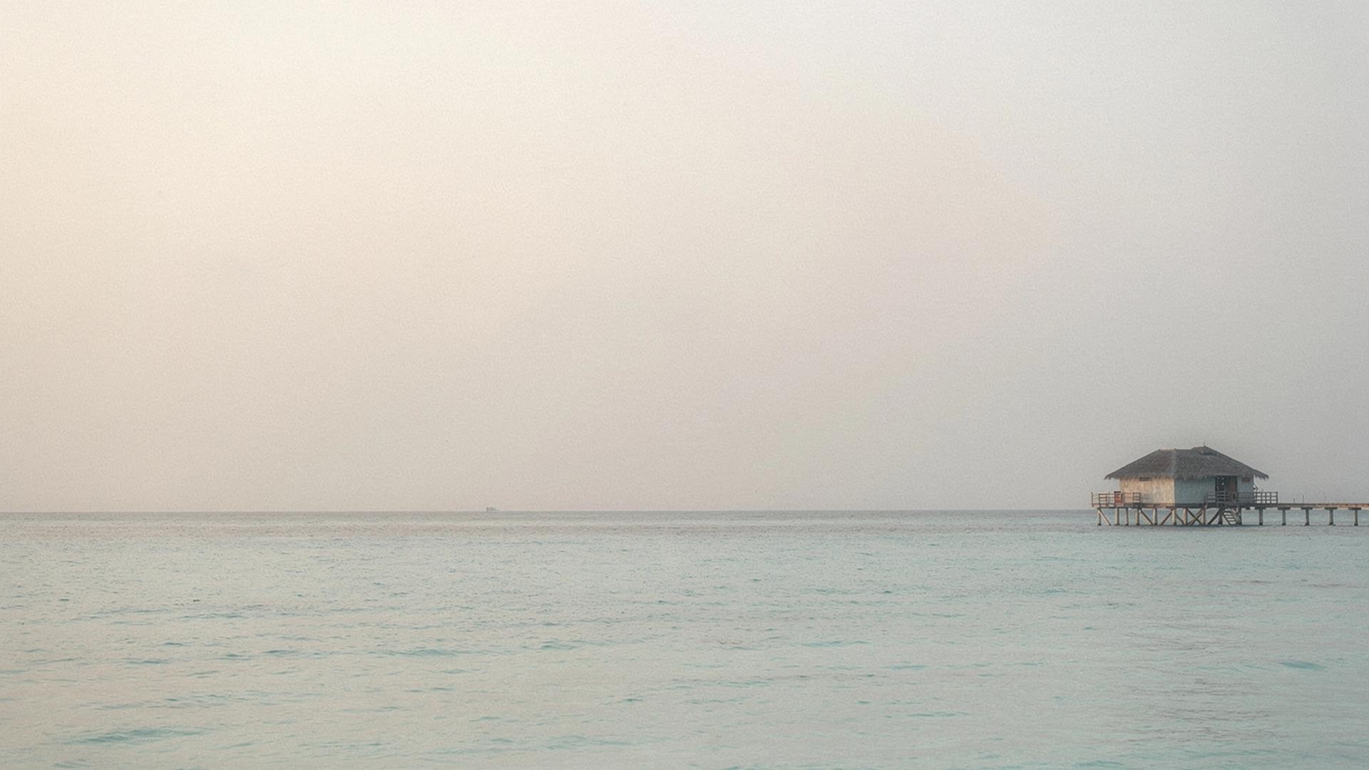 Calm Maldives lagoon at first light with a straight horizon line and one overwater villa on the right