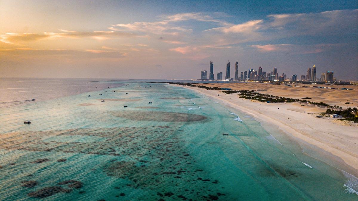 Aerial view of a Maldivian reef lagoon beside a Dubai shoreline at dusk