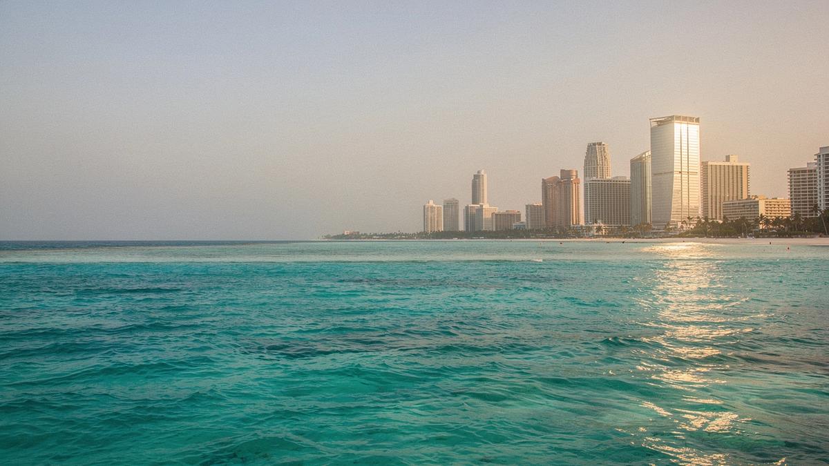 Lagoon water on the left of the frame meeting a Gulf city skyline on the right at golden hour